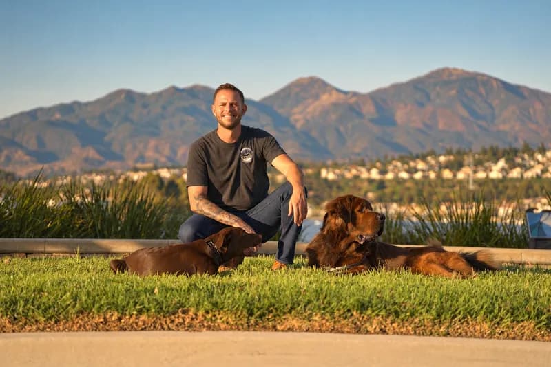 Kynos trainer Jake kneeling with two well-trained dogs on a hilltop